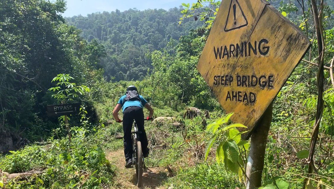 A rider passes a yellow sign that reads Warning, steep bridge ahead